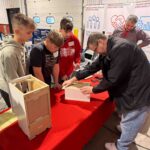 Group of kids surrounding a table with a man demonstrating construction techniques.