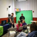 Two men presenting on graphics, audio/visuals to a group of kids.