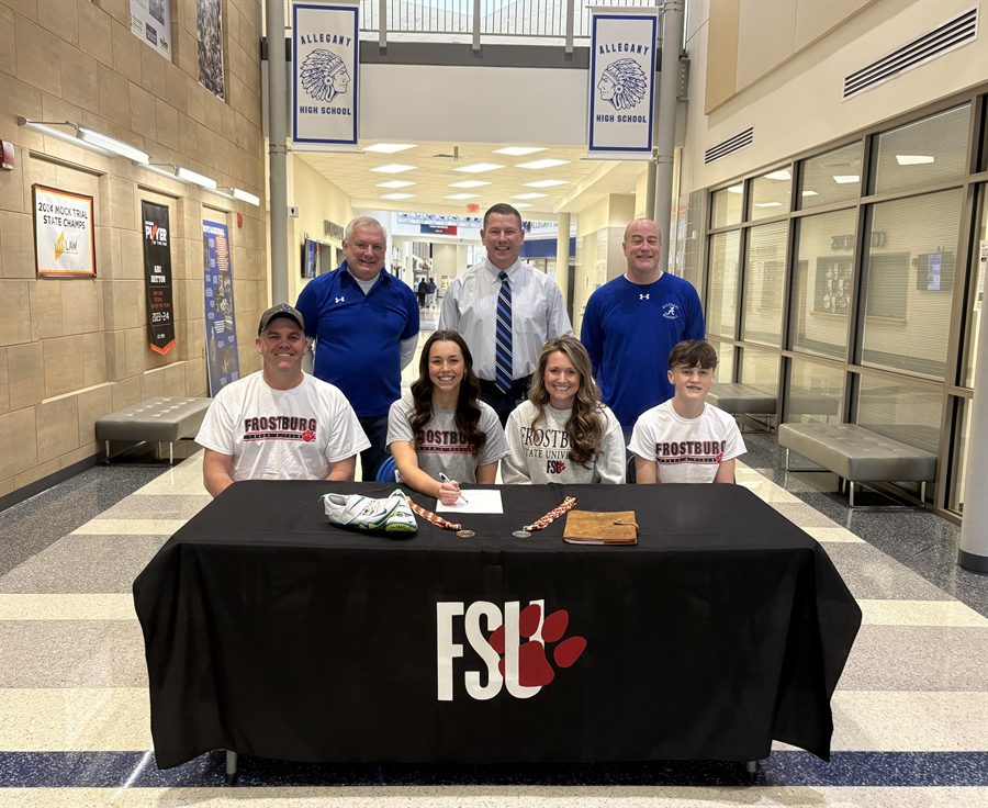 Photo of a student sitting at a table with others and three more men standing behind them.