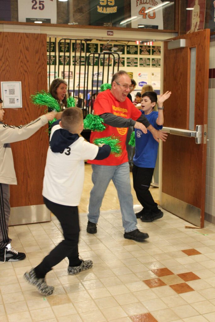 Photo of students with green pom-poms and a man smiling walking through.