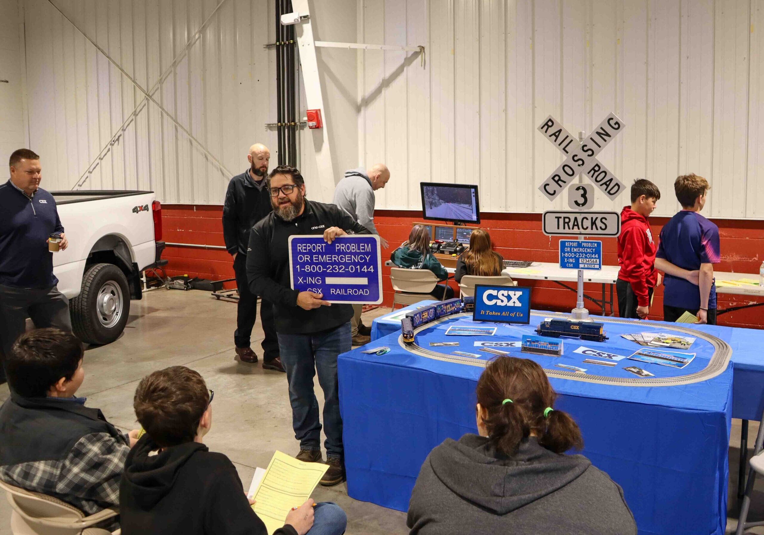 Students watching a man present with a train set up on a table.